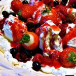 Fruit Pavlova! A delicious, easy dessert with a mix of berries, ice cream, whipped cream sitting in a crisp meringue, and topped off with a fruit ripple sauce.